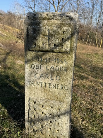 Cippo commemorativo di Carlo a Trattenero, con iscrizioni e simboli, immerso nella natura circostante.