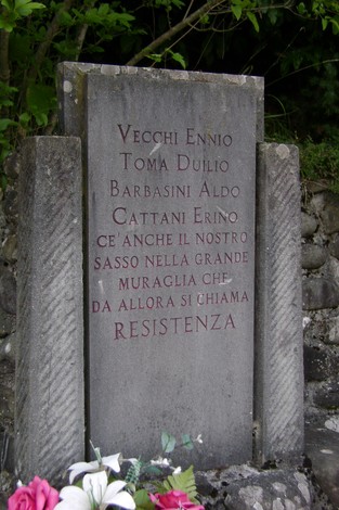 Monumento alla Resistenza con iscrizioni commemorative, circondato da vegetazione.