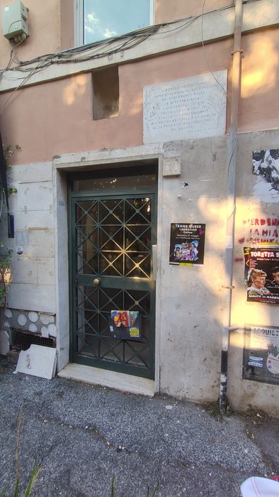 Lapide commemorativa apposta su un edificio, situata accanto a un ingresso con una porta verde.