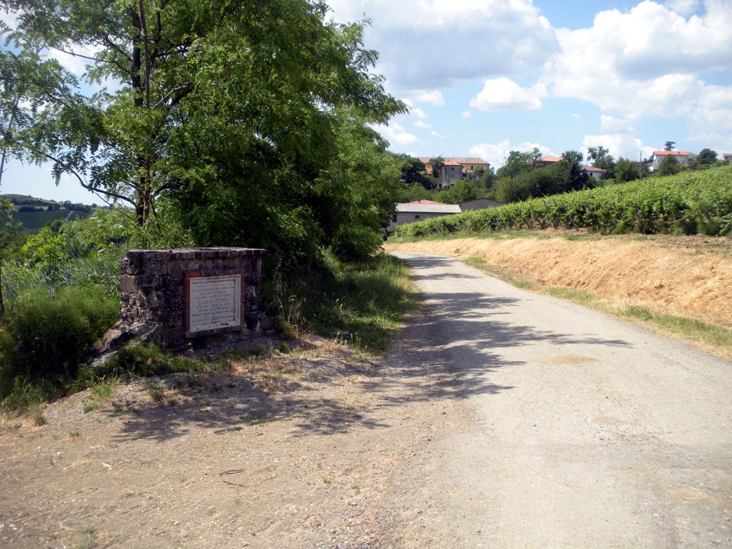 Monumento a Deniri, situato lungo una strada di campagna, circondato da natura e vigneti.