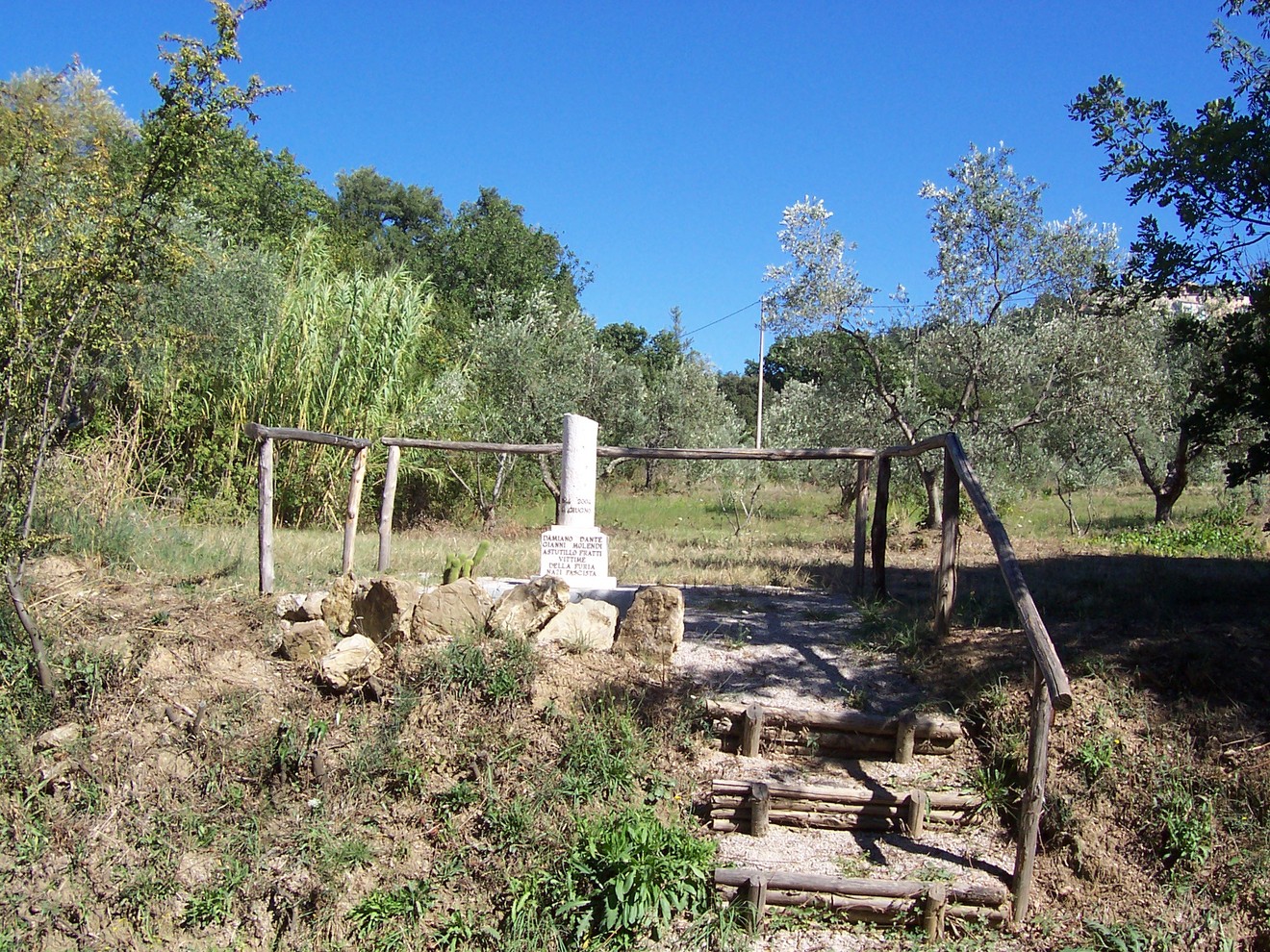 Cippo del podere di Grancaia, monumento in un paesaggio verdeggiante con ulivi e cereali.