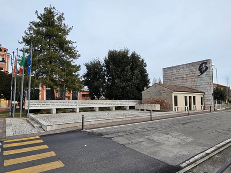 Monumento per l'eccidio di Villamarzana, con struttura architettonica e bandiere. Ambito commemorativo e storico.