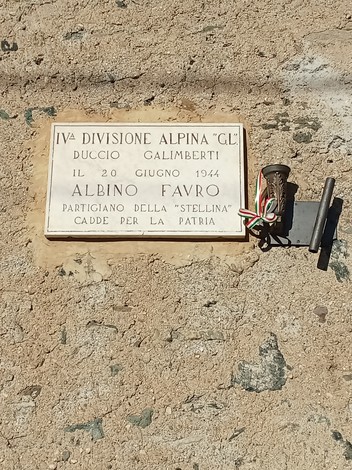Lapide commemorativa dedicata ad Albino Favro, partigiano caduto per la patria, su sfondo di pietra.
