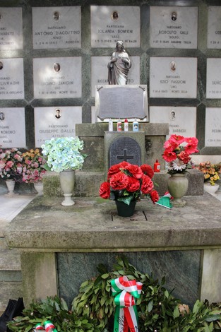 Rappresentazione del "Sacrario dei caduti per la Liberazione" con fiori, candele e una statua commemorativa.