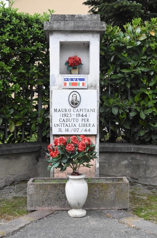 Cippo commemorativo dedicato a Mauro Capitani, caduto per l'Unità d'Italia, con fiori e stemma tricolore.