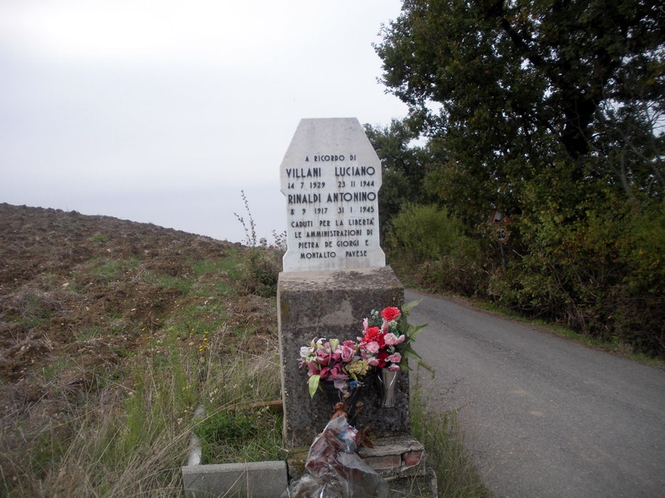 Cippo commemorativo dedicato a Villani e Rinaldi, immerso in un paesaggio rurale.