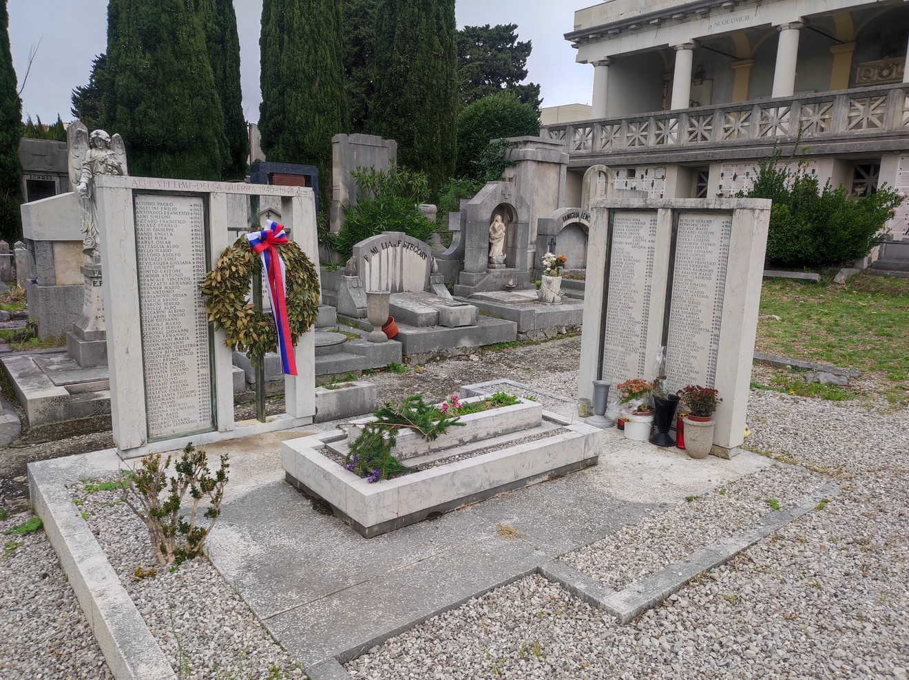 Sacrario dei caduti per la Libertà, con monumento e iniziali di onore ai defunti, circondato da piante e fiori.