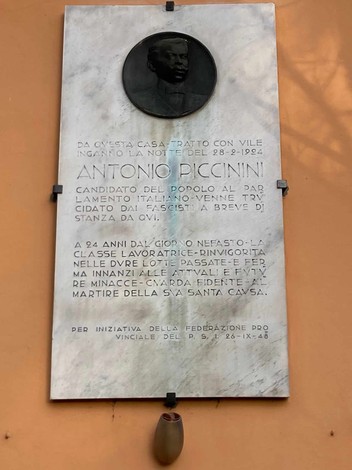 Lapide commemorativa dedicata ad Antonio Piccinini, situata su un muro in un contesto urbano.