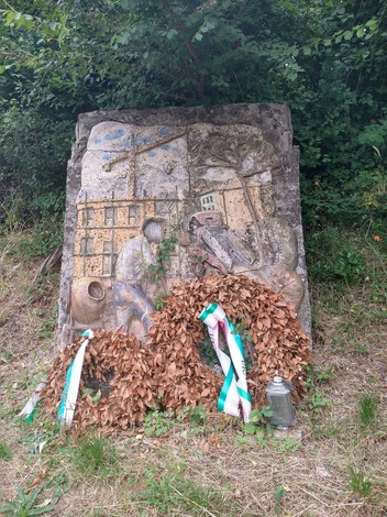 Monumento dedicato a Moggi e Fissi, con decorazioni e ghirlande di foglie nel contesto naturale circostante.