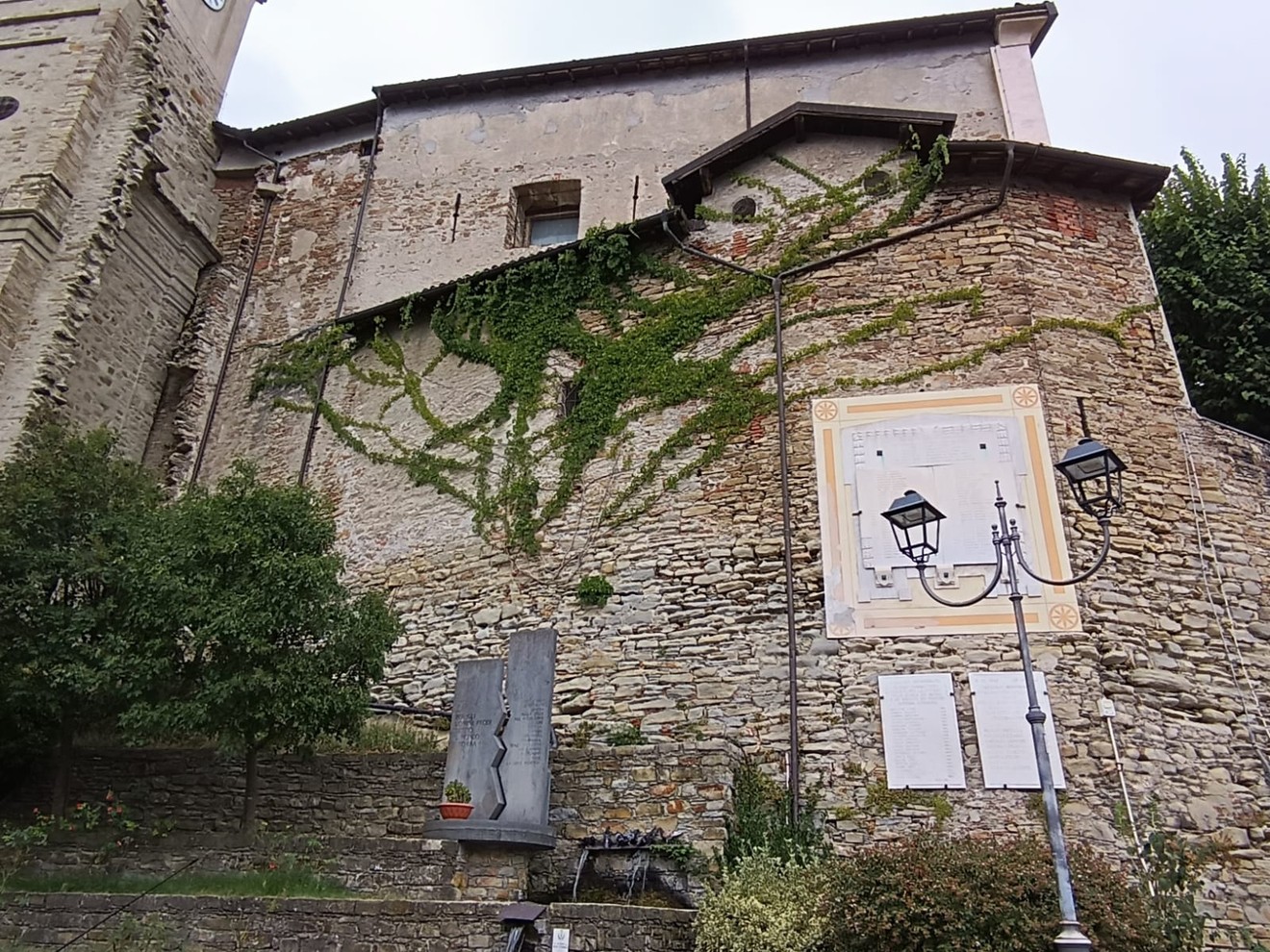 Monumento ai caduti di Tagliolo Monferrato, con alle spalle un edificio storico e vegetazione che lo avvolge.