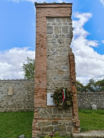 Cimitero di Casaglia, con monumento e pareti in pietra, immerso nel verde e nel cielo blu.