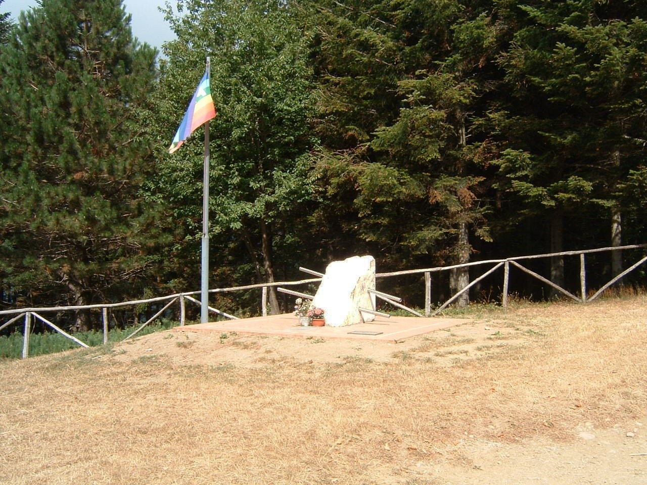 Monumento del passo degli Acandoli, situato in un'area boschiva, con bandiera e base decorata.