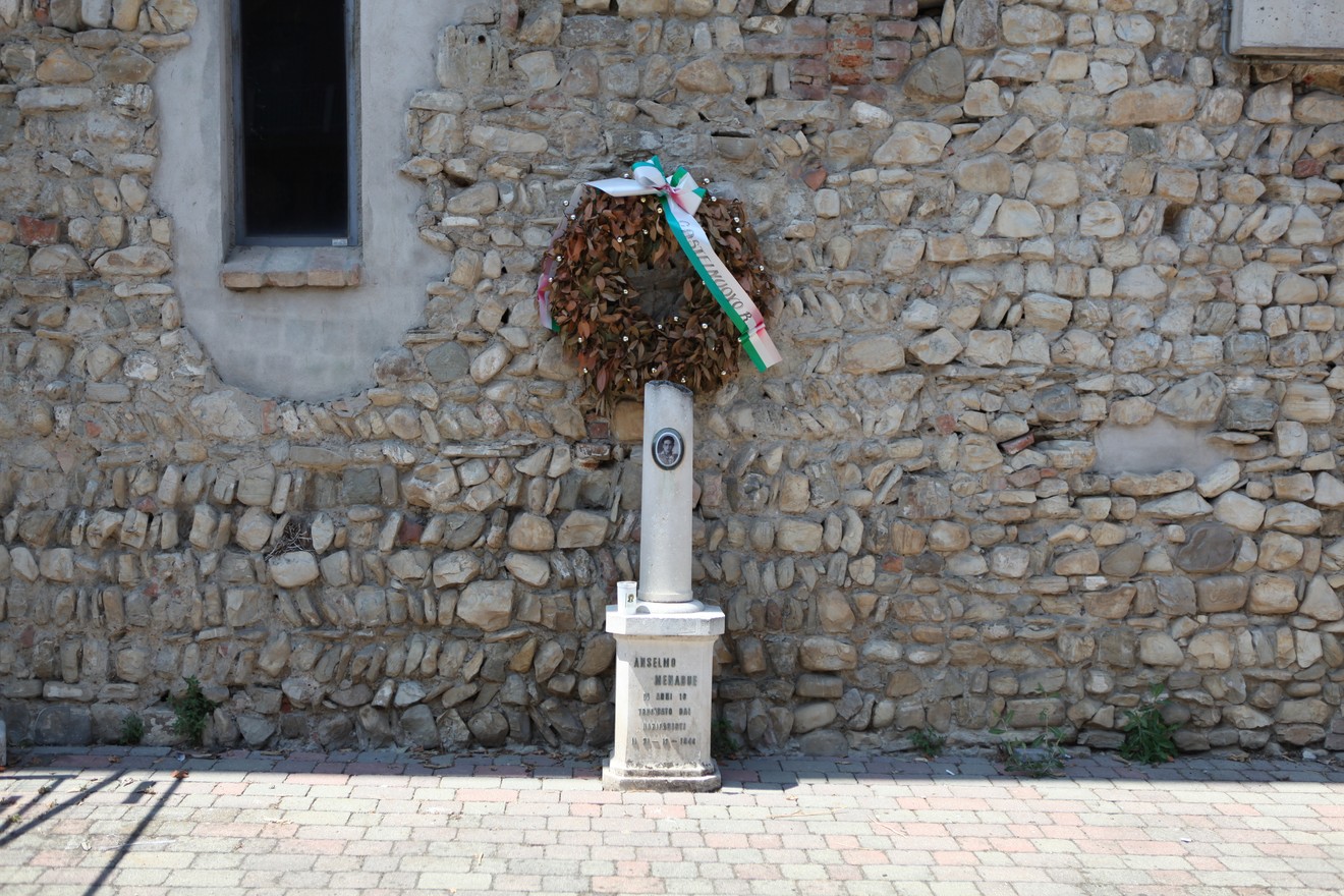 Cippo commemorativo con corona d'alloro su muro di pietra, simbolo di memoria storica e rispetto.