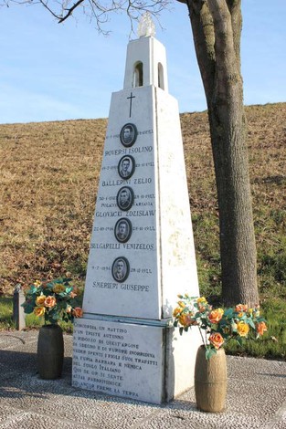 Cippo commemorativo con nomi incisi, decorato con fiori, situato in un'area verde.