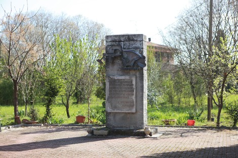 Monumento commemorativo dedicato ai caduti del Tiro a segno, situato in un giardino verdeggiante.