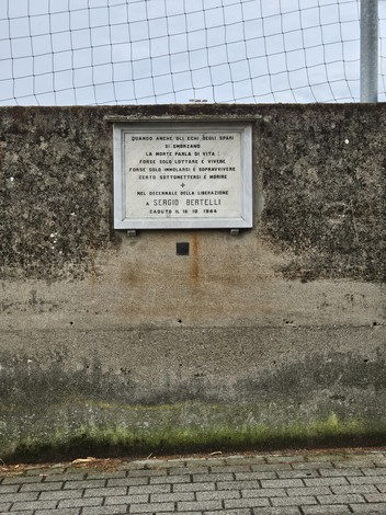 Lapide commemorativa dedicata a Sergio Bertelli, situata su un muretto in un contesto esterno.