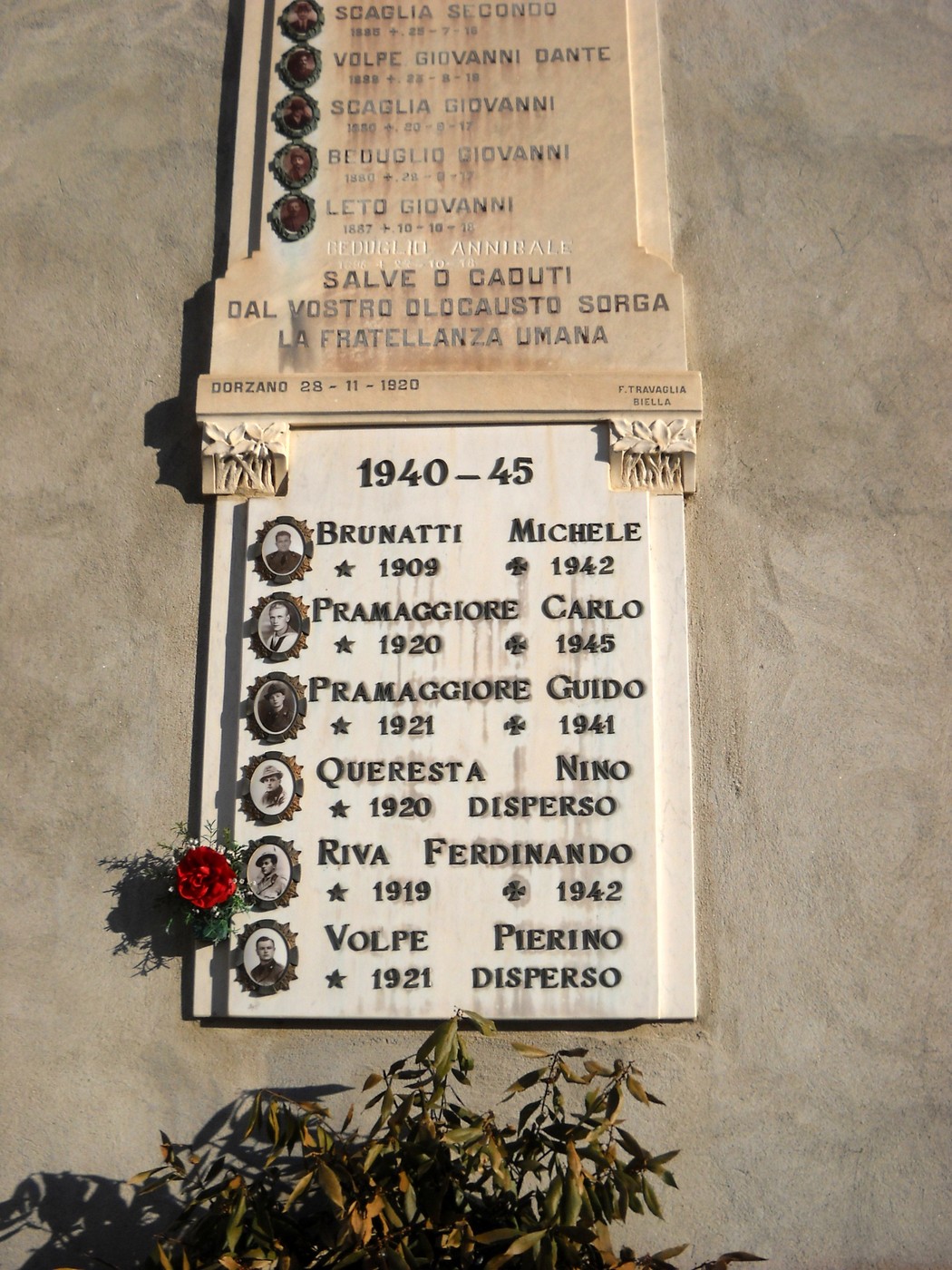 Lapide commemorativa dedicata ai caduti della Seconda Guerra Mondiale, con nomi e date. Fiore rosso in omaggio.