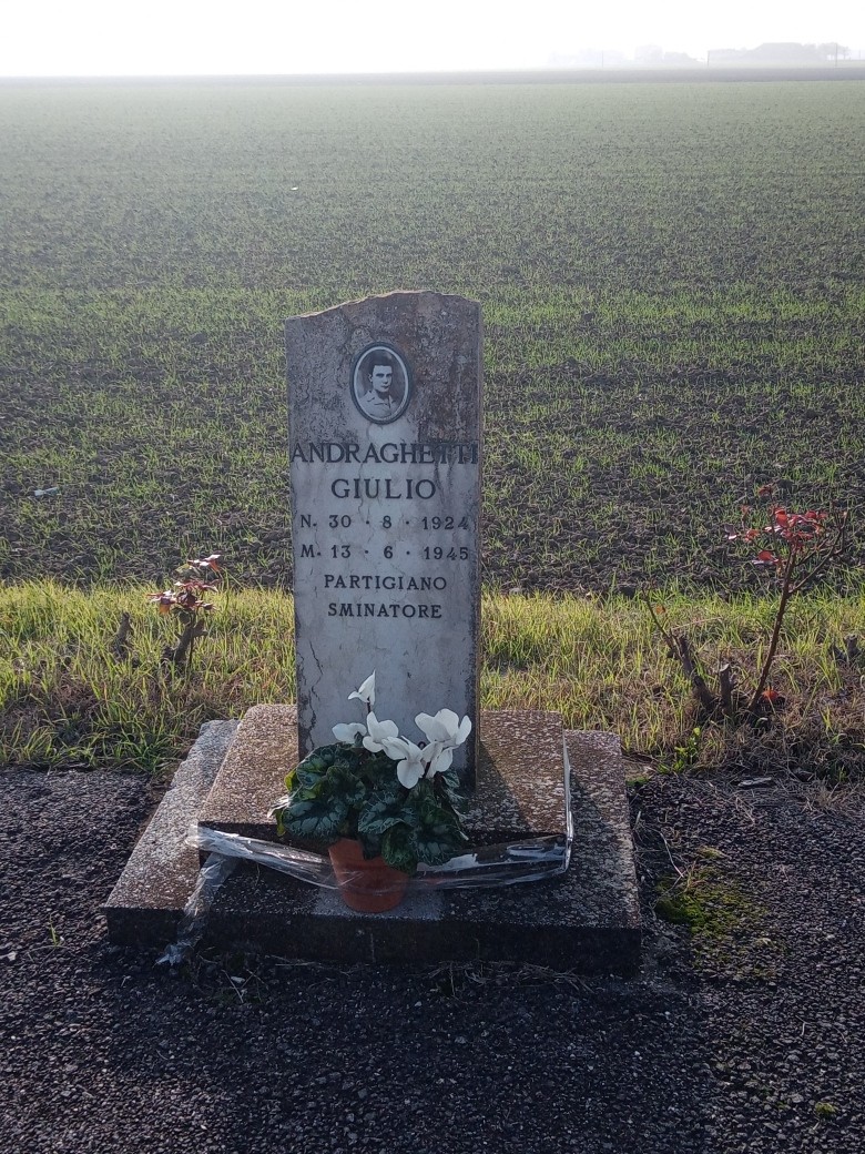 Cippo dedicato a Giulio Andraghetti, partigiano, con fiori in un campo. Memoriale di memoria storica.