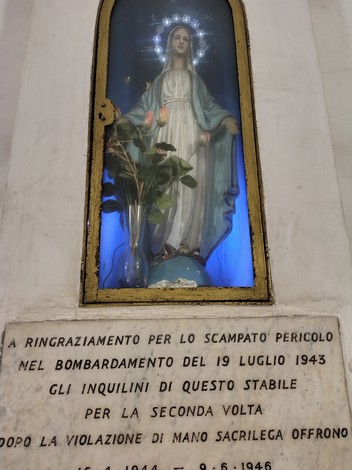 Statua della Madonna, illuminata, con dedica al bombardamento del 19 luglio 1943 e un ramoscello di rosa.