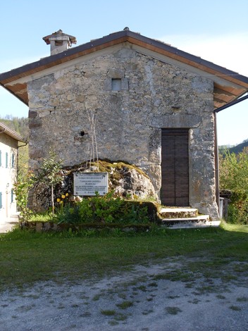 Lapide commemorativa a Ludescher e Roser, su una casa in pietra circondata da natura.