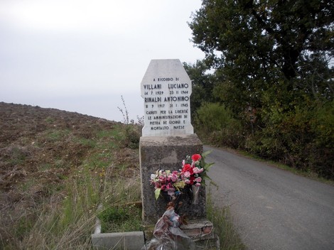 Cippo commemorativo dedicato a Villani e Rinaldi, immerso in un paesaggio rurale.