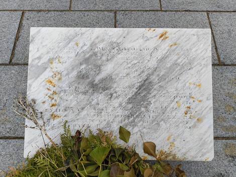 Lapide commemorativa in un cimitero militare italiano, circondata da foglie essiccate e riflessi di luce.