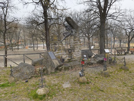 Monumento ai caduti di Botteghino di Zocca, circondato da alberi, con statue e candele commemorative.
