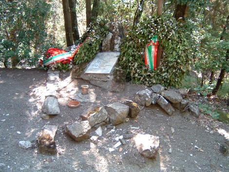Cippo commemorativo dedicato ai caduti di Radio Cora, circondato da decorazioni e piante nel bosco.
