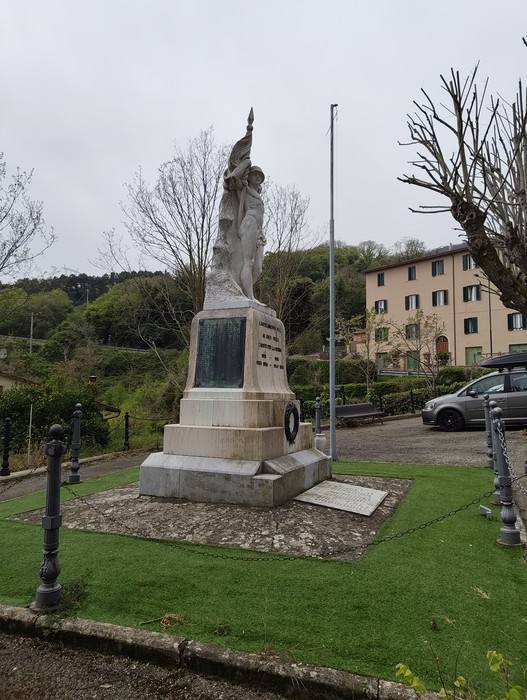 Monumento ai caduti, raffigurante una figura alata su una base monumentale, circondato da verde e edifici.