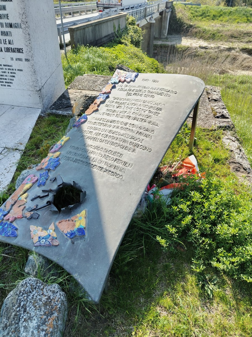 Lastra commemorativa dedicata agli sminatori, visibile in un contesto naturale e circondata da vegetazione.