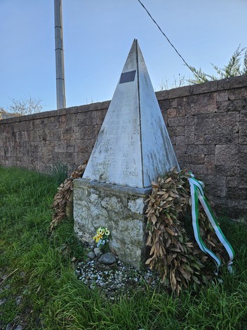 Monumento ai Martiri di Ressora, obelisco con decorazioni floreali e foglie, immerso nel verde.
