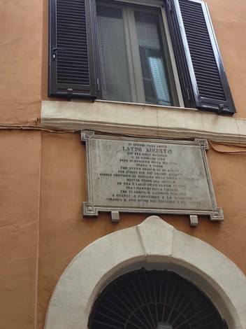 Lapide commemorativa dedicata a Latini, affissa su un edificio caratteristico. Dettagli storici e architettonici visibili.