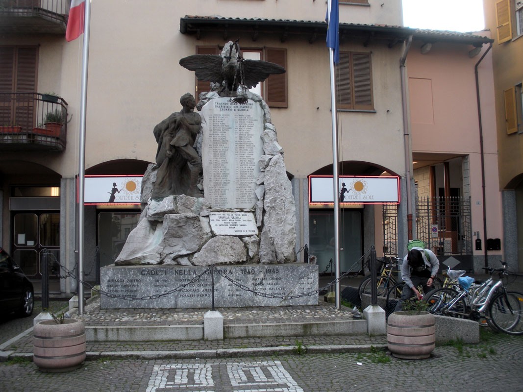 Monumento ai caduti di Gropello Cairoli, dedicato alla memoria dei soldati, circondato da bandiere e biciclette.