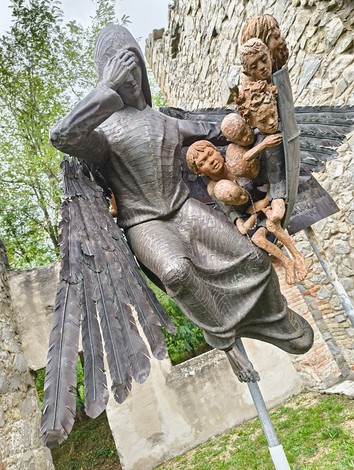 Scultura angelica con bambini, immersa tra le rovine dell'oratorio di Cerpiano, simbolo di vita e speranza.