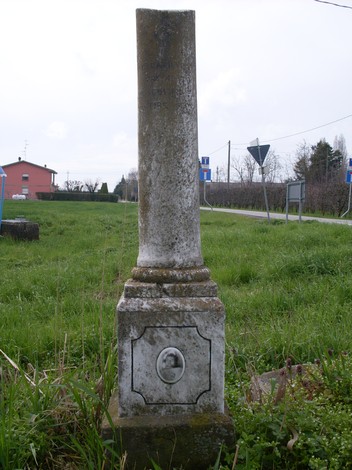 Cippo commemorativo dedicato a un partigiano ignoto, immerso nel verde, lungo una strada.