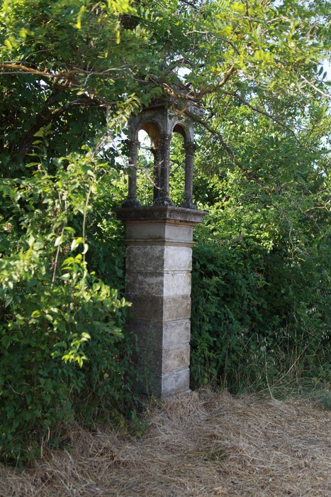 Cippo commemorativo ai caduti, circondato da vegetazione in un paesaggio naturale.
