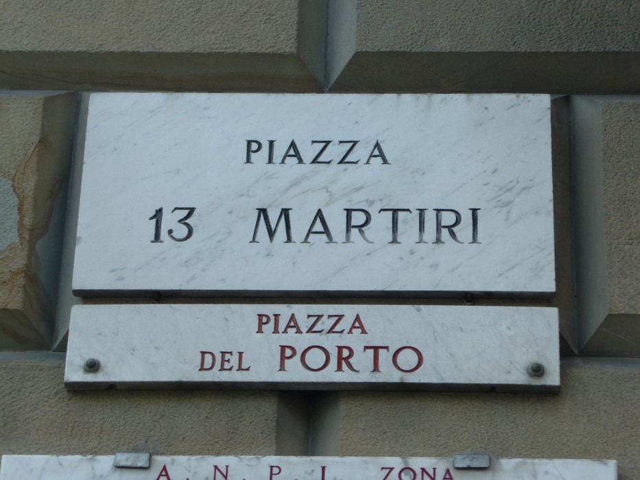 Targa che indica "Piazza 13 Martiri" e "Piazza del Porto" su fondo marmoreo.