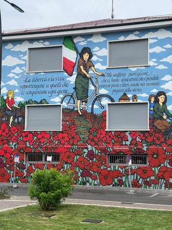 Murale che celebra le staffette partigiane, simbolo di libertà e resistenza, adornato da fiori rossi.