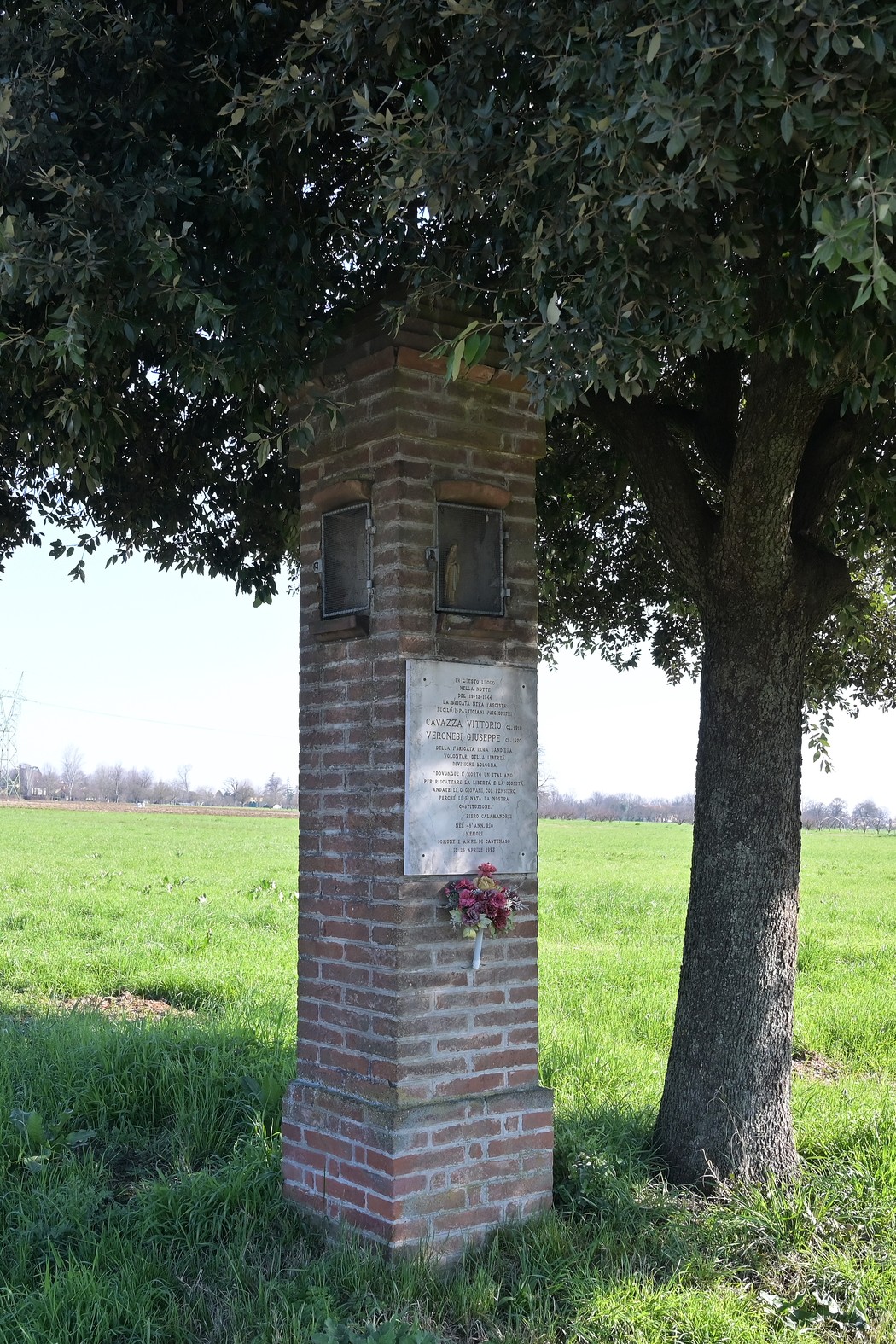 Cippo in mattoni circondato da un albero, al centro di un campo verde, commemorativo di Cavazza e Veronesi.