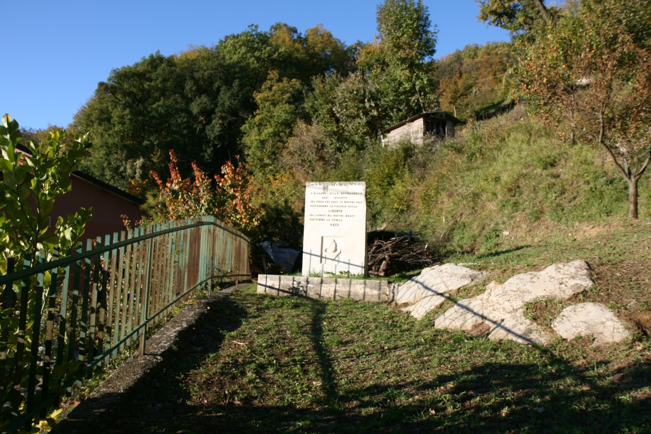 Monumento commemorativo dedicato all'incendio di Fontia, immerso nel verde, con una stele su terreno erboso.