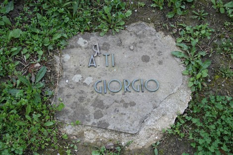 Monumento commemorativo nel cimitero di Stia, dedicato a Giorgio, immerso nella vegetazione.