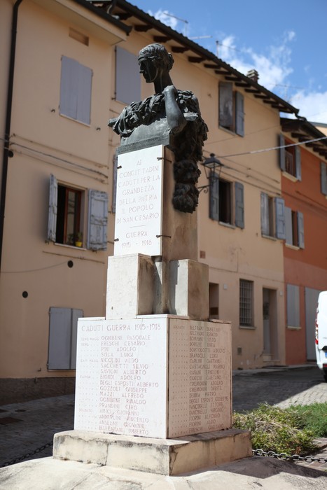 Monumento ai Caduti con busto e iscrizioni commemorative, situato in un contesto urbano.