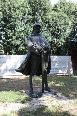 Monumento ai Caduti con statua di soldato in uniforme, circondato da vegetazione e pannelli informativi.