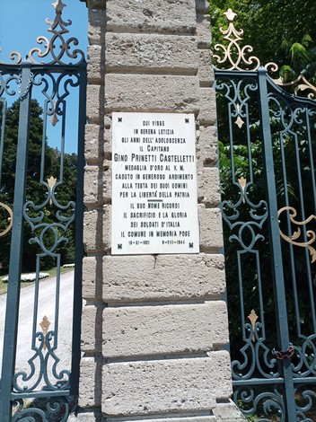 Lapide commemorativa dedicata a Gino Prinetti Castelletti, posta su una recinzione in pietra.