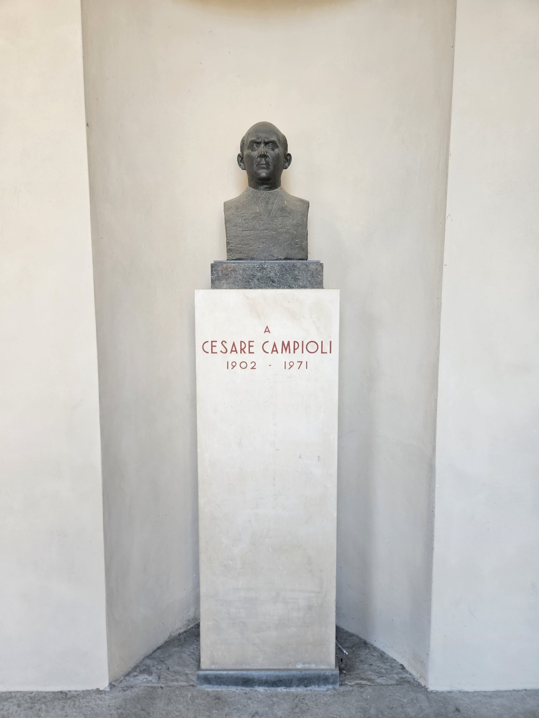 Busto di Cesare Campioli, affiancato da una base con iscrizione, in un ambiente sobrio e illuminato.