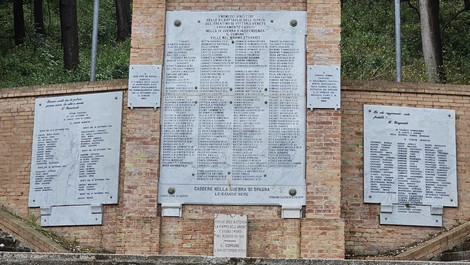 Monumento ai caduti con targa commemorativa e nomi dei caduti in guerra, incorniciato da bosco.