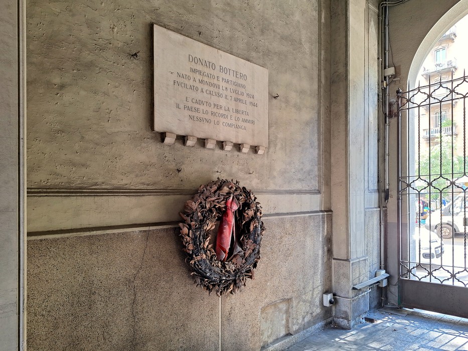 Lapide commemorativa in memoria di Donato Bottero, decorata con una corona di fiori, all'interno di un edificio.