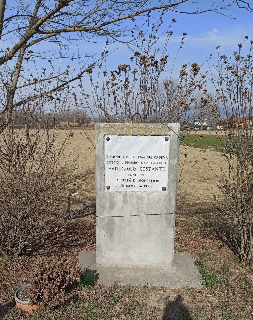 Cippo commemorativo a Panizzolo, dedicato ai caduti, circondato da un paesaggio rurale.