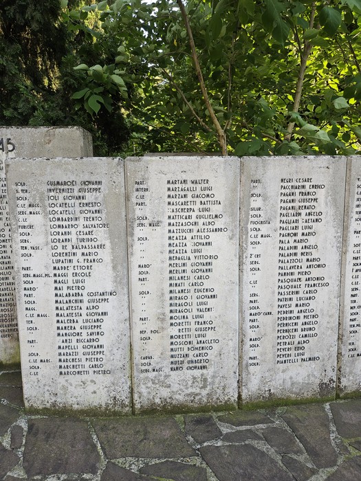 Monumento ai Caduti con una fila di nomi incisi su lastre di pietra, in un contesto verde e tranquillo.