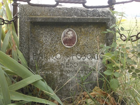 Cippo commemorativo dedicato a Franco Foscato, decorato da un'immagine e circondato da vegetazione.